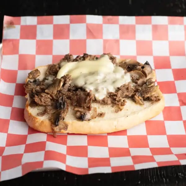 Cheesesteak sandwich with melted cheese, steak, and mushrooms on a red and white checkered paper.