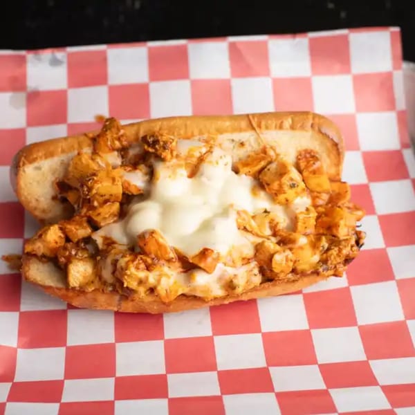 A chicken cheesesteak sandwich with melted white cheese on a red and white checkered paper.