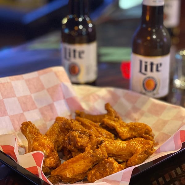 A basket of Valentino's NY Pizza's buffalo wings with two bottles of Miller Lite in the background.
