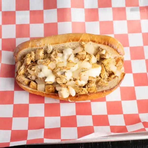 Chicken cheesesteak sandwich with melted cheese and onions on a red and white checkered paper.