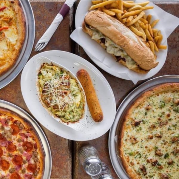 Valentino's NY Pizza spread with two pizzas, a cheesesteak and fries, and a baked pasta dish.