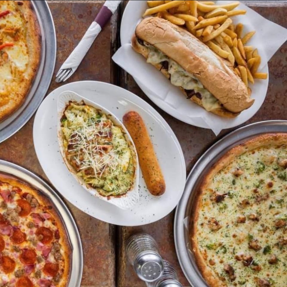Valentino's NY Pizza spread with two pizzas, a cheesesteak and fries, and a baked pasta dish.
