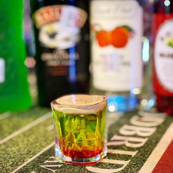 A colorful layered shot glass sits on a green surface resembling a football field.