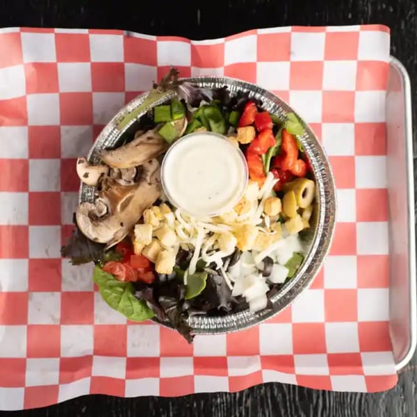 Overhead view of a salad in a foil bowl with various toppings and a cup of dressing.